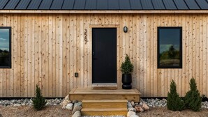 A wooden cabin with a black door, numbered 3587, and two windows. - Hidden Acres - Austur Cabin (Petoskey)