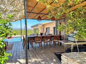 A covered outdoor dining area with a pool, wooden deck, and a view of the landscape.
