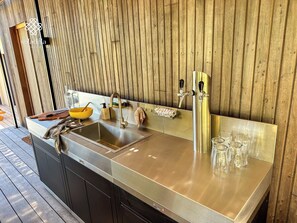 A modern kitchen with a stainless steel sink, a wooden wall, and a wooden cutting board.