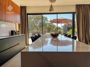 A modern kitchen with a large island, a dining area with a glass table, and a view of the outdoors.