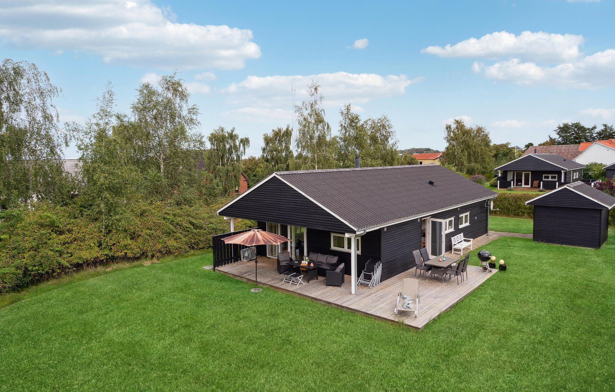 Een zwart huis met een terras, een patio en een kleine schuur.