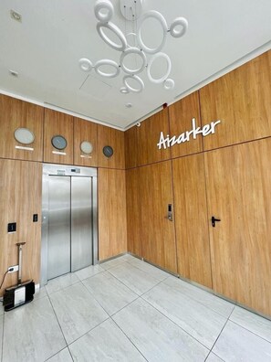 Un ascensor moderno con detalles metálicos, una pared de madera con una placa y un piso cubierto de baldosas limpias.