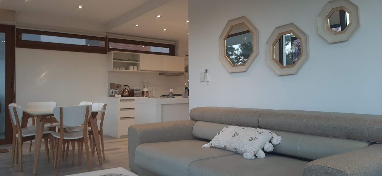 A modern living room with a grey sofa, a white plush toy, and a dining area with wooden chairs and a white table.