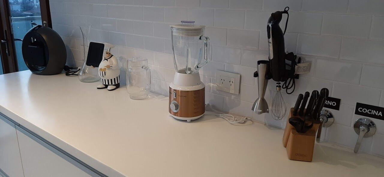 Una cocina con encimera blanca, licuadora, cafetera, bloque de cuchillos y salpicadero con la palabra "Cocina".