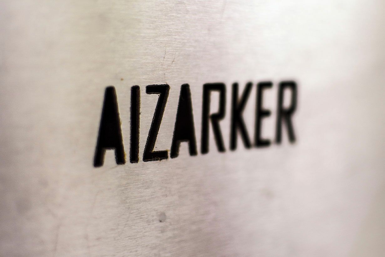 Primer plano de la palabra "AIZARKER" sobre una superficie metálica.
