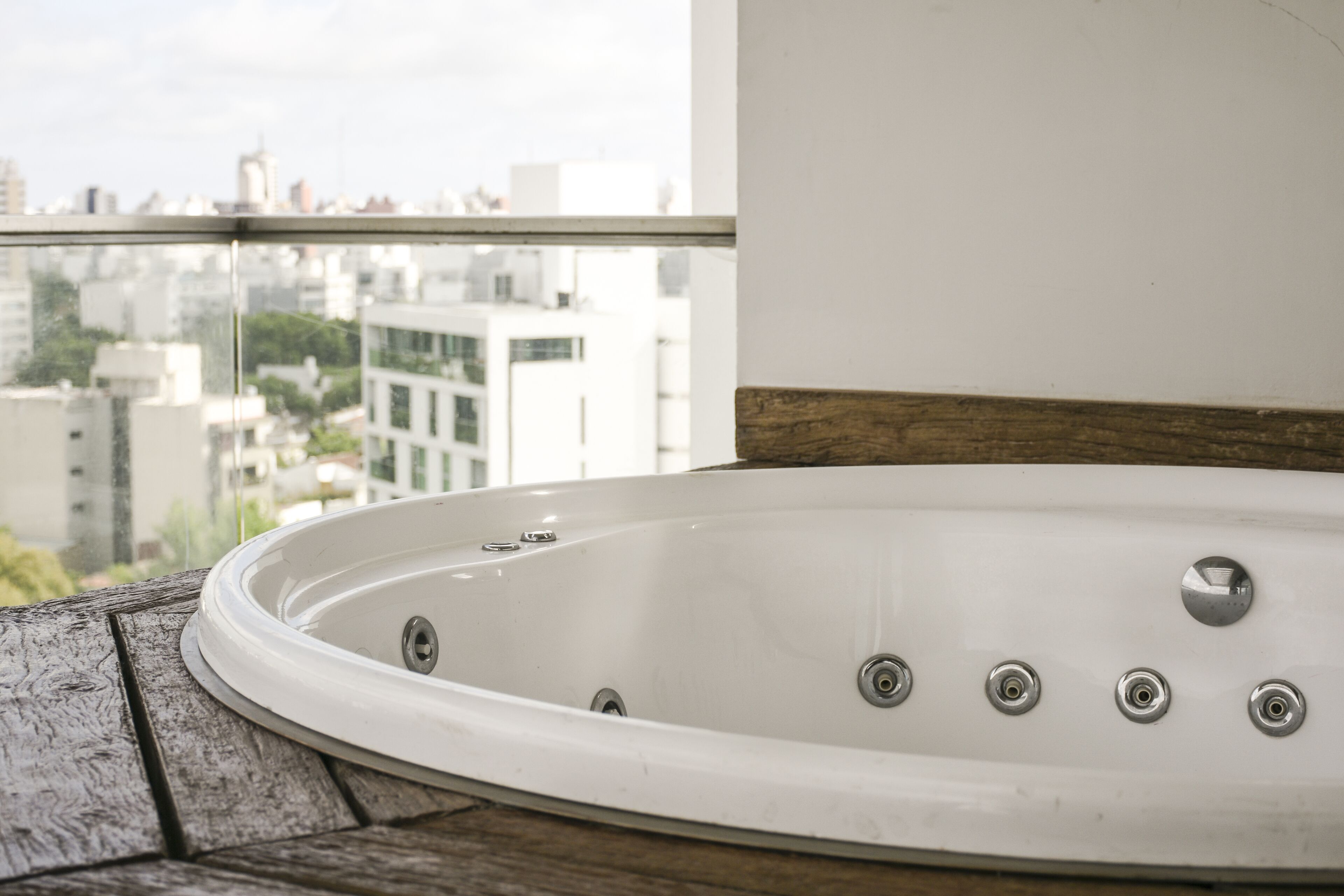Un bain à remous avec une terrasse en bois et une vue sur la ville, visible à travers une fenêtre.