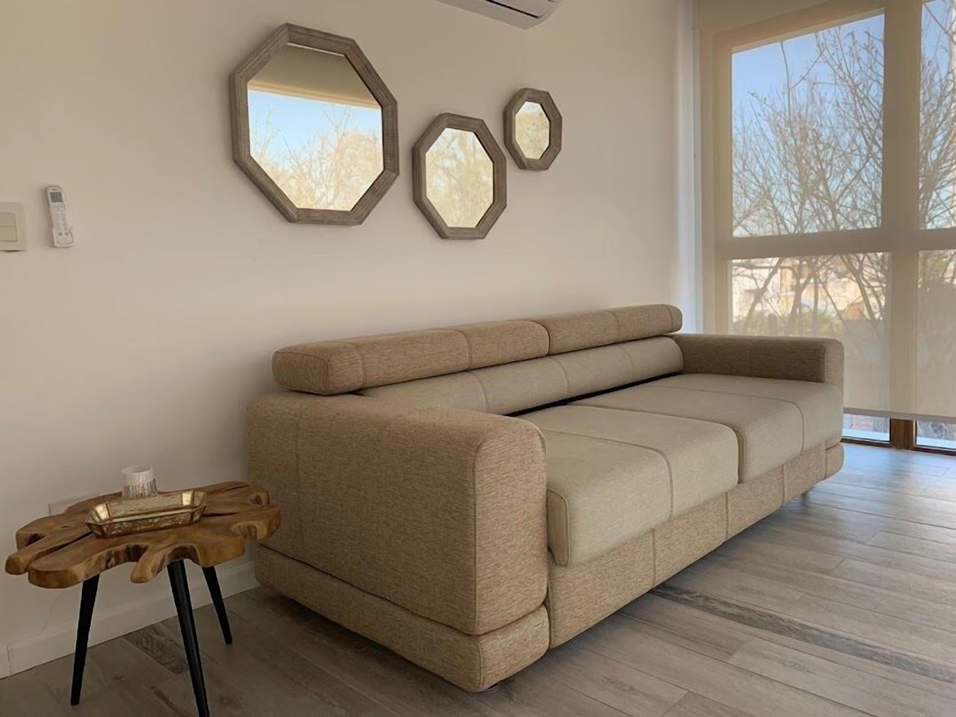 A modern living room with a beige sofa, wooden coffee table, and three hexagonal mirrors on the wall.