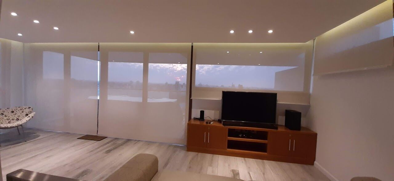 Un moderno salón con un televisor de pantalla plana grande, mueble de madera para entretenimiento y un ventanal con vistas al horizonte de la ciudad.