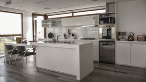 Una cocina moderna con armarios blancos, una isla central, electrodomésticos de acero inoxidable y vistas a través de un amplio ventanal.