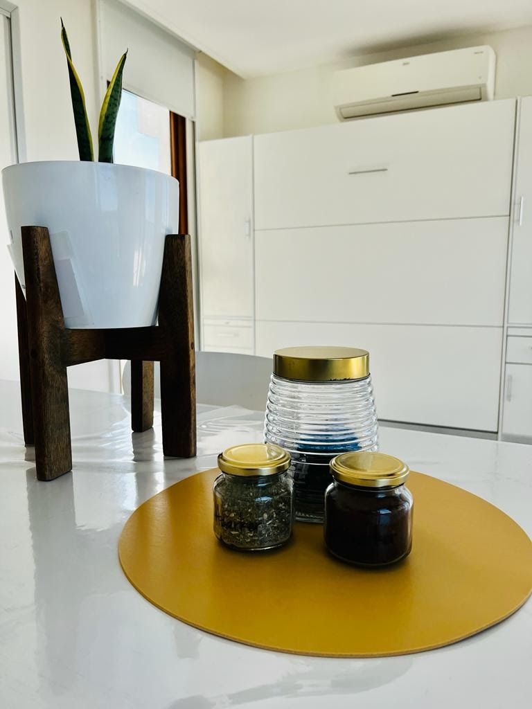 Una cucina moderna con mobili bianchi, una pianta in vaso e tre barattoli con tappi dorati su un tavolo giallo.