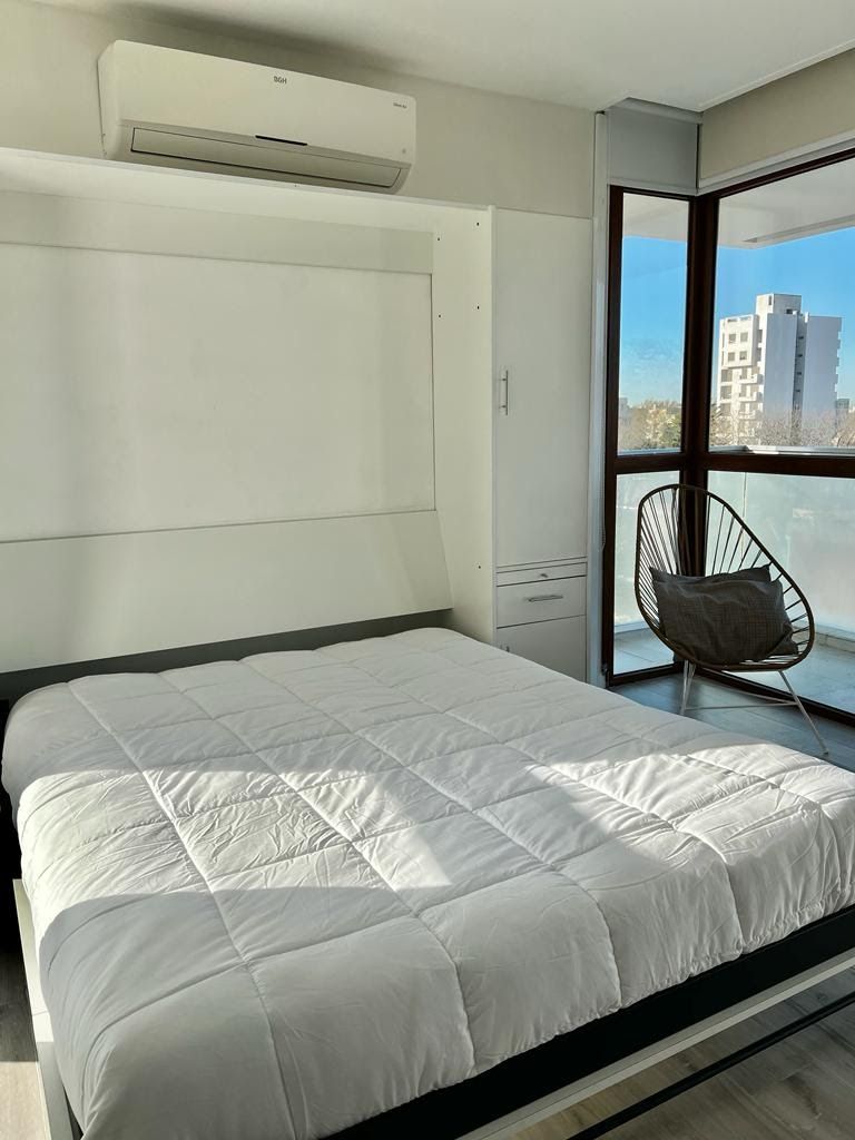A modern bedroom with a large bed, a chair, and a view of buildings through a window.