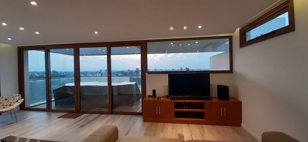 A spacious living room with a large sliding glass door leading to a balcony, a flat-screen TV, and a wooden entertainment unit.