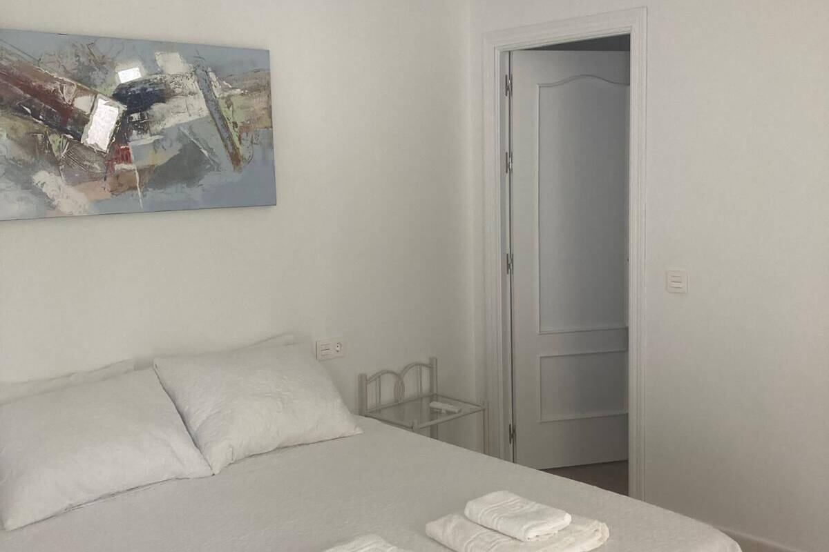 A bedroom with a bed, a ceiling fan, a door, and a wall-mounted abstract painting.