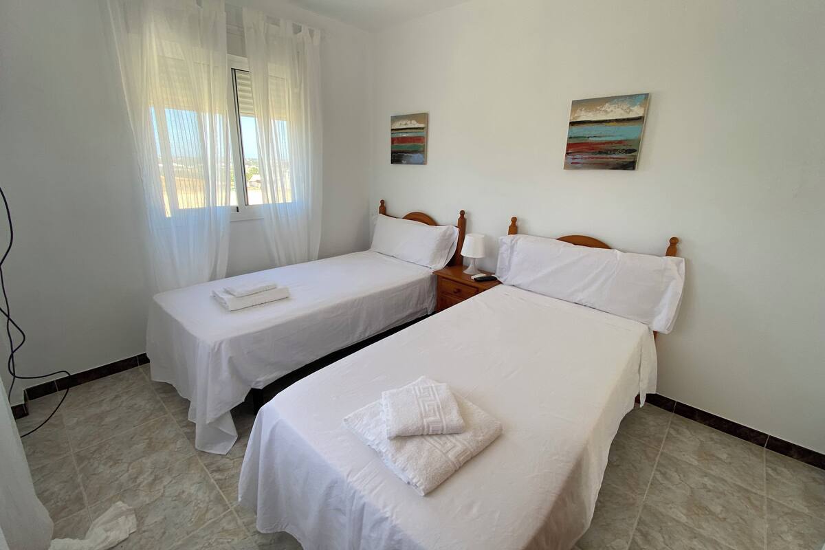 A hotel room with two single beds, a ceiling fan, and two paintings on the wall.