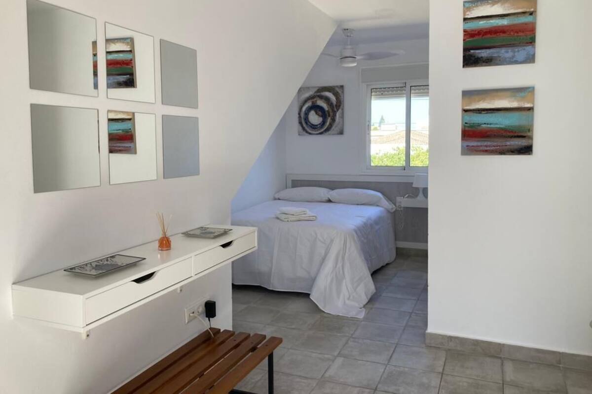 A bedroom with a bed, a bedside table, a bench, a dresser, and artwork on the walls.