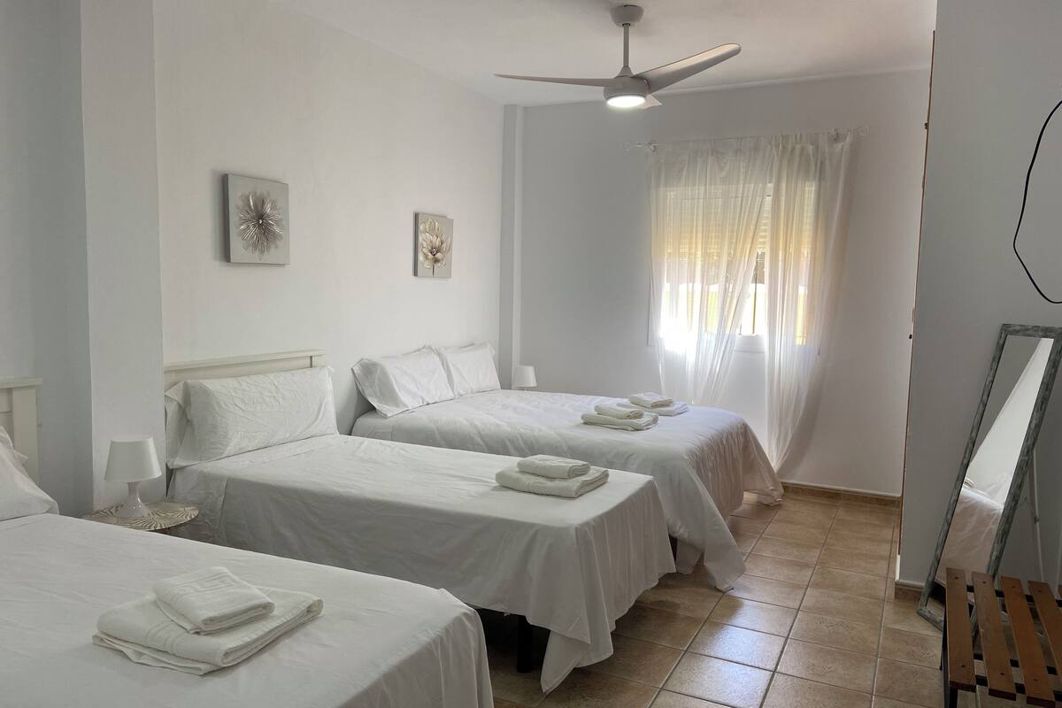 A hotel room with two beds, white bedding, a ceiling fan, and a window with sheer curtains.