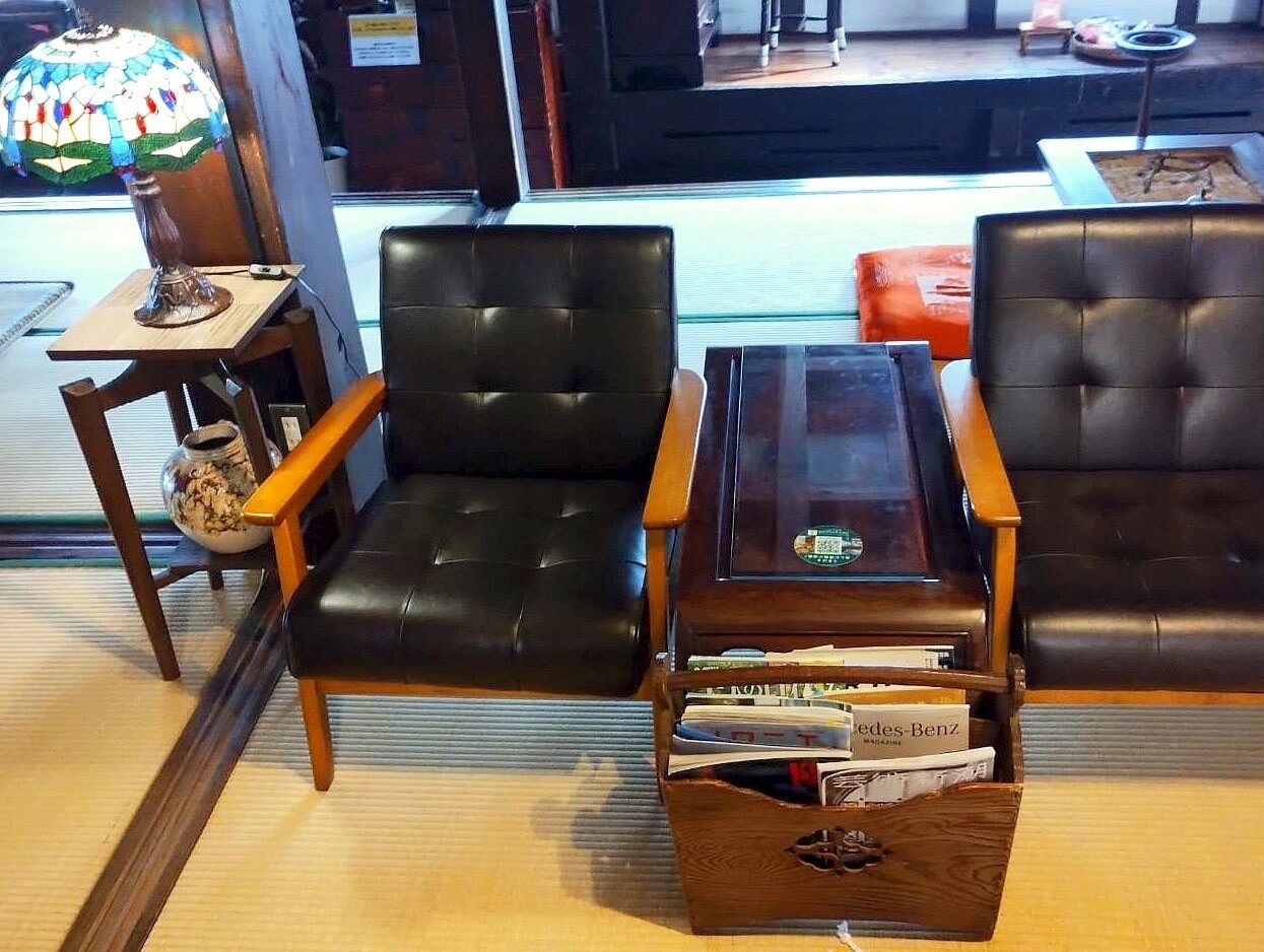 A room with two black leather chairs, a wooden coffee table with magazines, and a small table with a lamp.