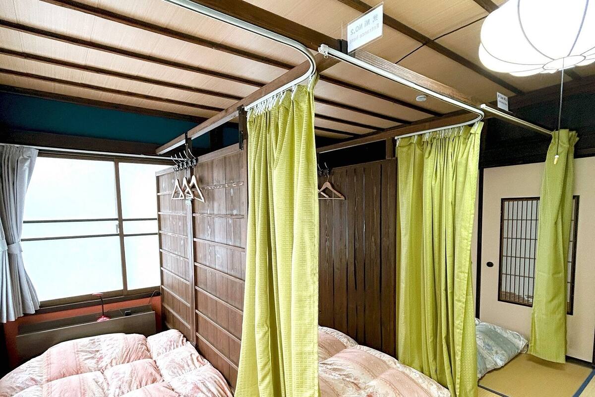 A traditional Japanese-style room with tatami flooring, a futon bed, a wooden wardrobe, and a window with curtains.