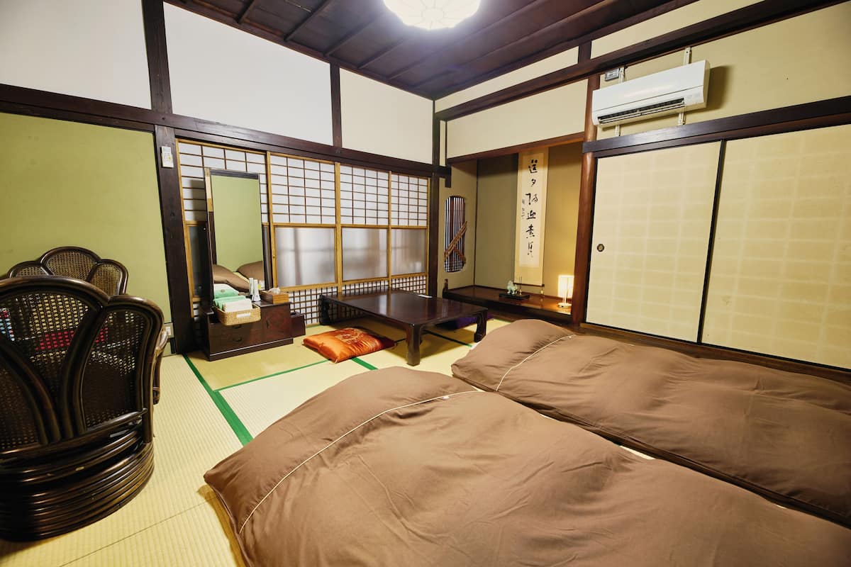 A traditional Japanese room with tatami flooring, a low table, a sofa, and a seating area with chairs.