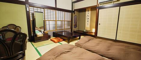 A traditional Japanese room with tatami flooring, a low table, a sofa, and a seating area with chairs.