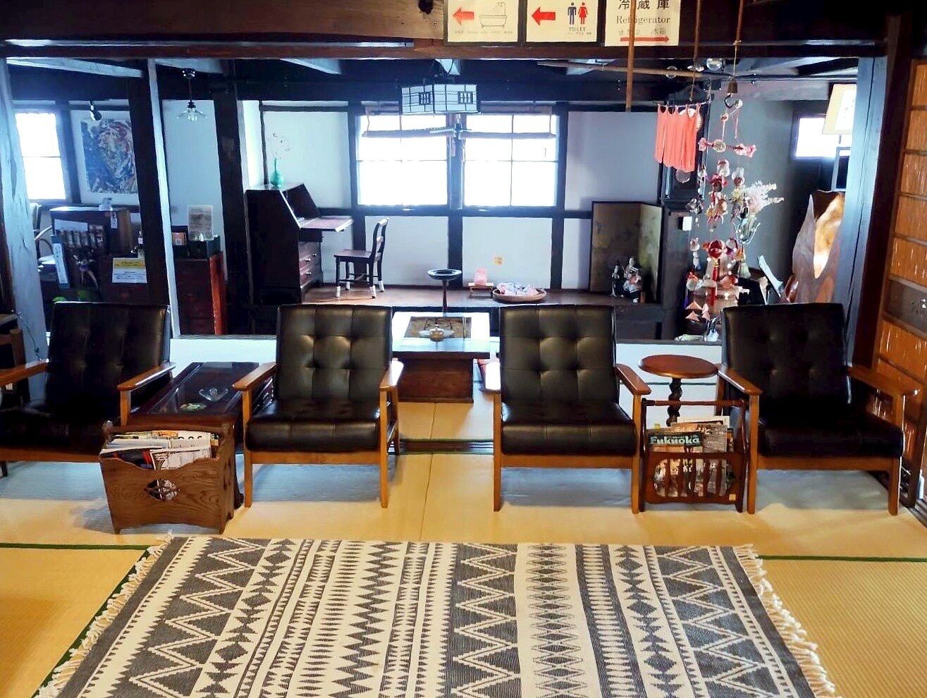 Una sala de estar tradicional japonesa con suelo de tatami, sofás de cuero negro, una mesa de centro de madera baja y un adorno colgante decorativo.