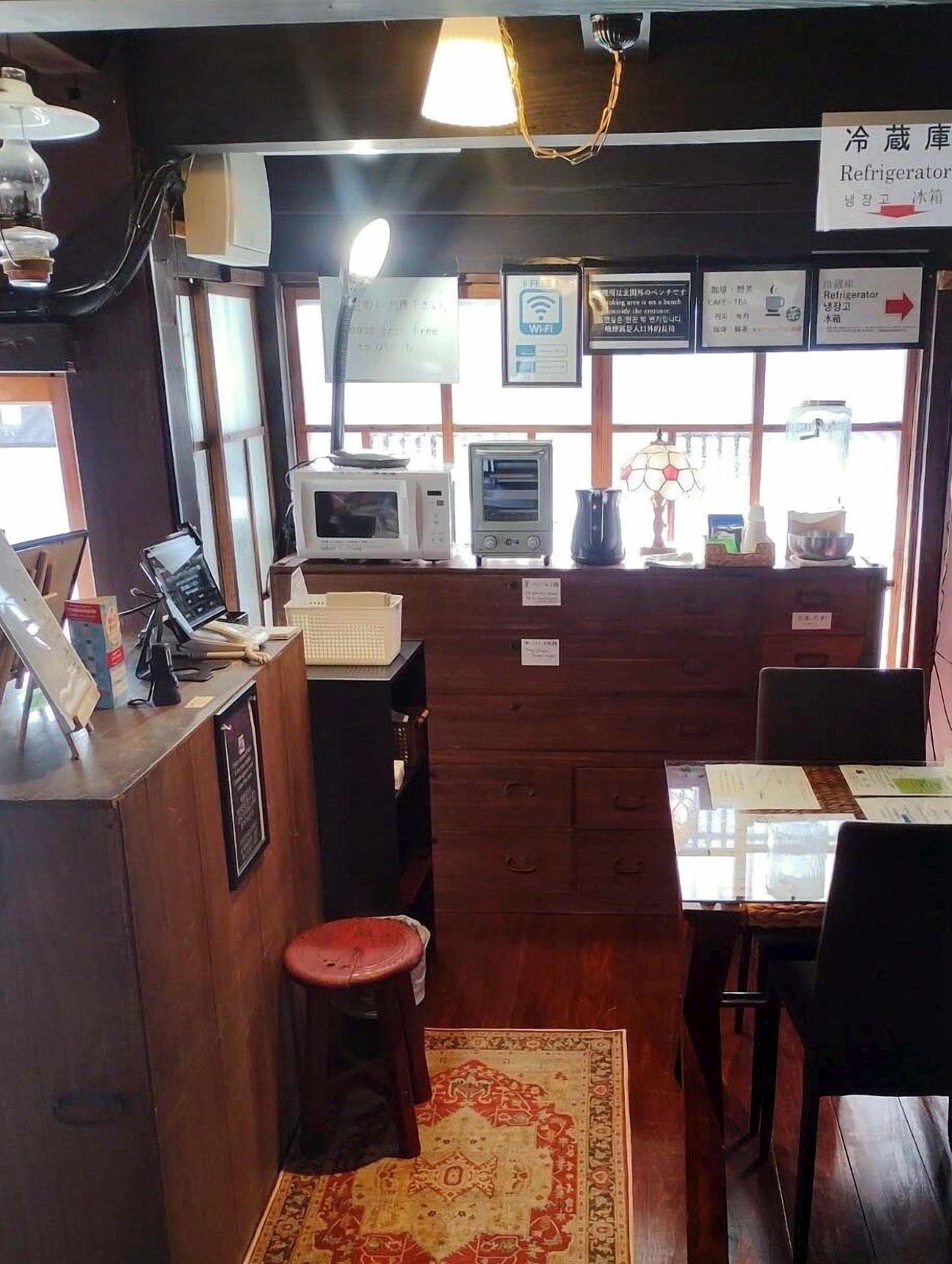 A restaurant interior with wooden furniture, a counter with a phone, a microwave, a toaster, and a refrigerator.
