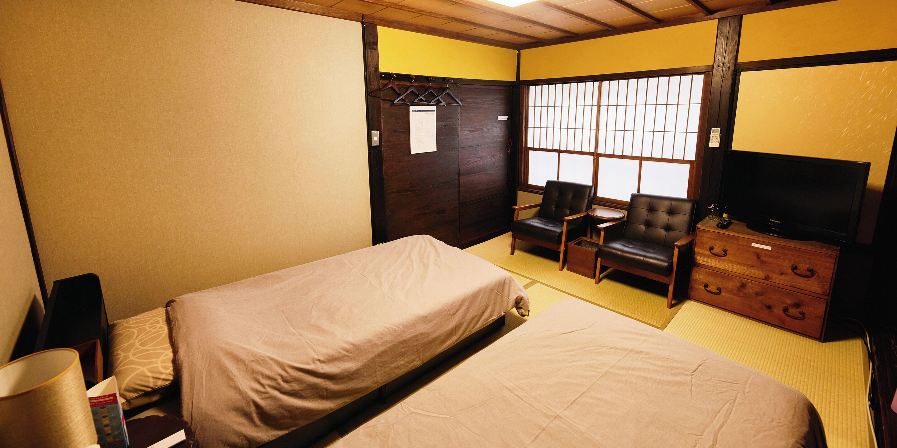 A hotel room with a bed, a TV, a wooden dresser, and a seating area with chairs and a small table.