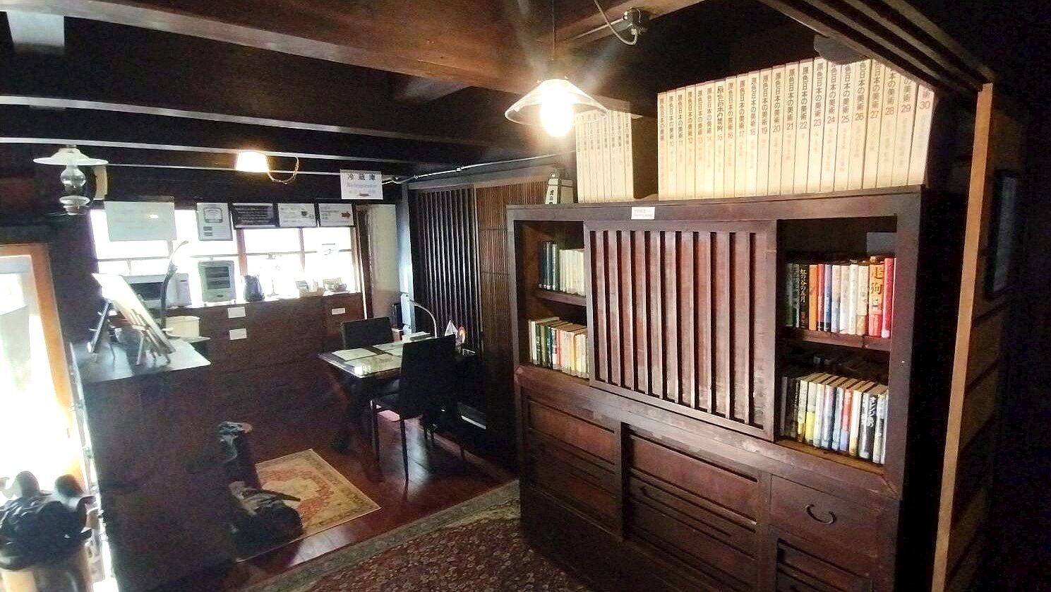 A room with a wooden bookshelf, a desk with a chair, and a small rug on the floor.