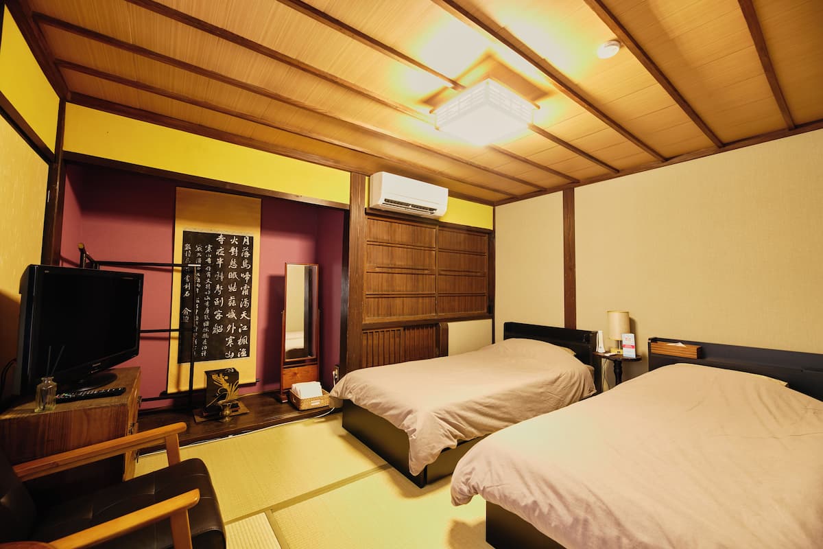 A hotel room with two beds, a television, a wooden ceiling, and an air conditioning unit.