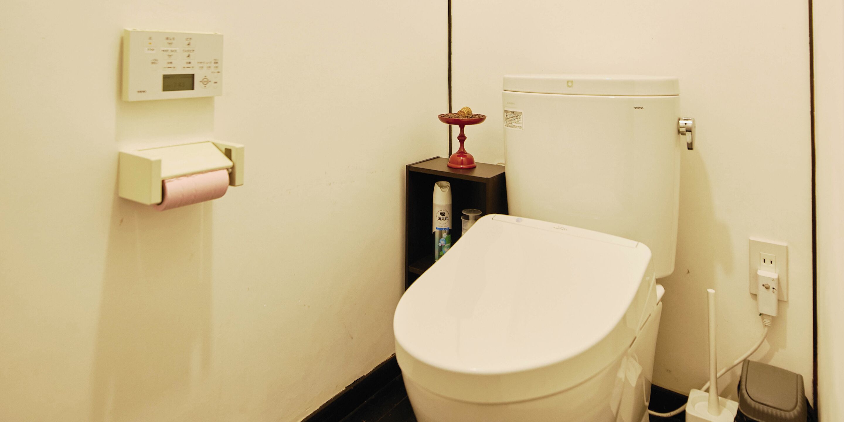Une petite salle de bain simple, équipée d’un WC, d’un porte-rouleau de papier toilette, d’un distributeur de savon et d’un chauffe-eau.