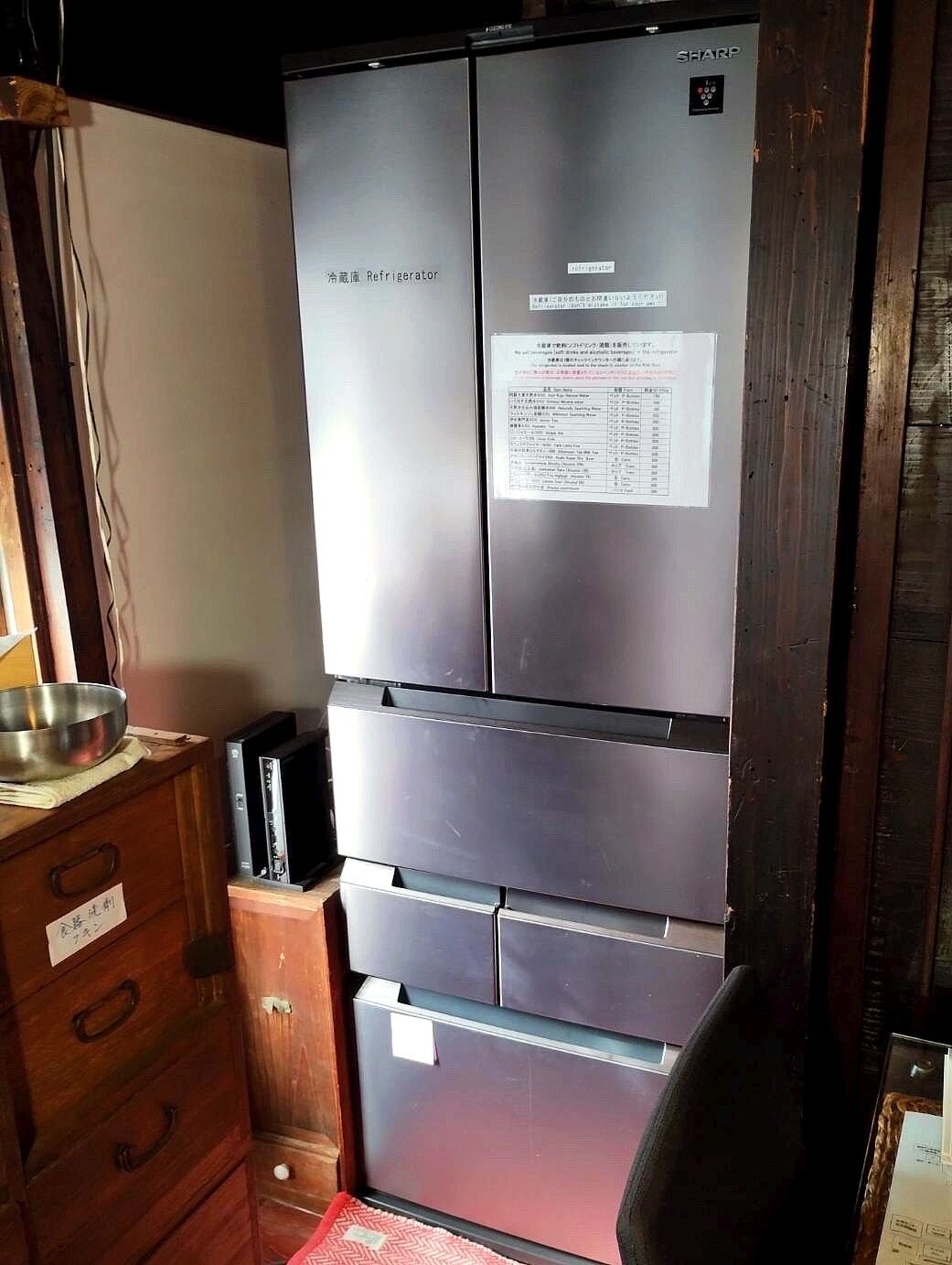 A compact kitchen with a stainless steel refrigerator, a microwave, and a wooden cabinet with a metal bowl on top.