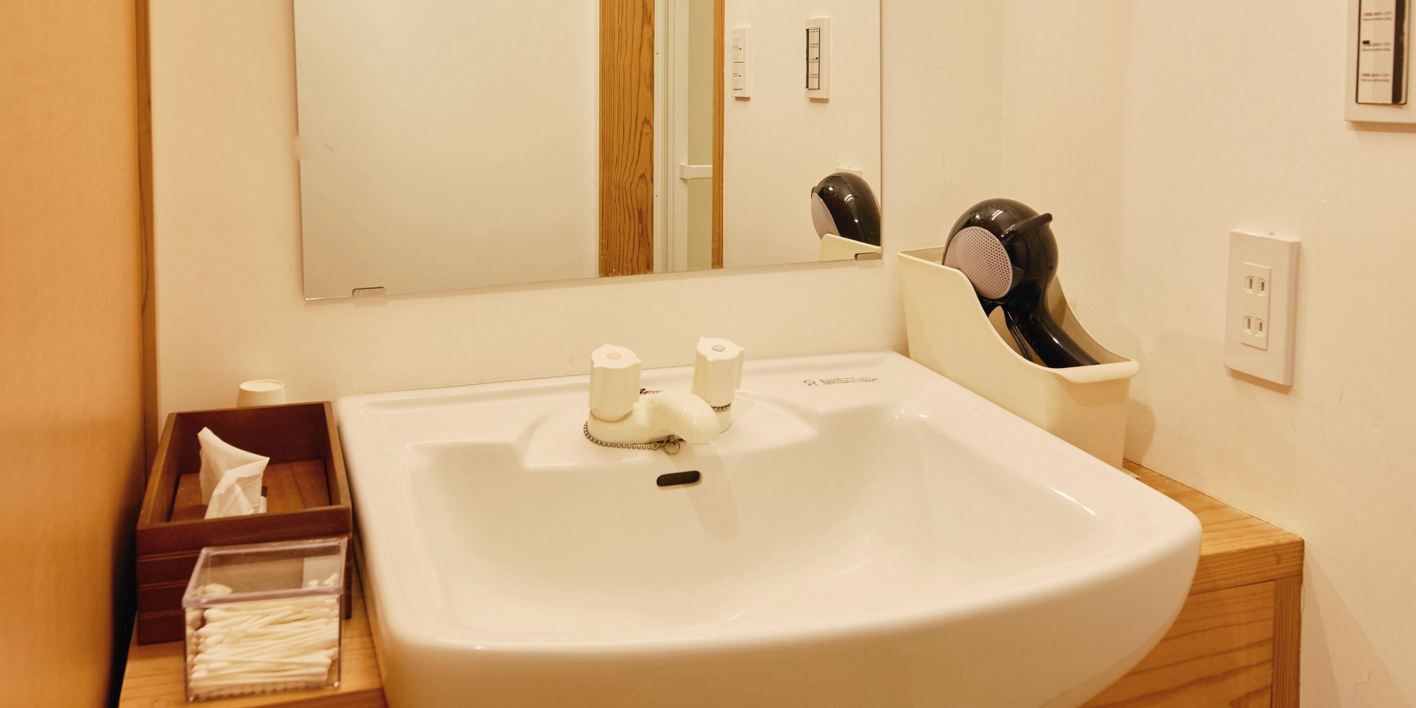 A bathroom with a white sink, a mirror, a hairdryer, and a tissue box.