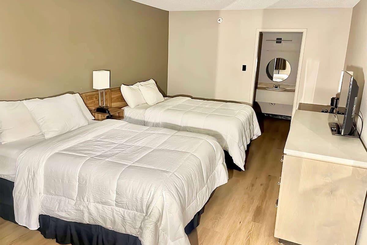 A hotel room with two beds, a bedside table with a lamp, a mirror, a TV, and a small cabinet.