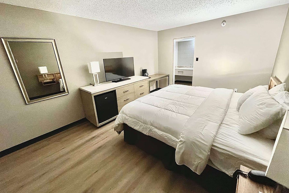 A hotel room with a bed, a desk with a TV, a mirror, and a wardrobe.