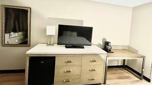 A hotel room with a flat-screen TV on a white desk, a coffee maker, and a mirror on the wall.