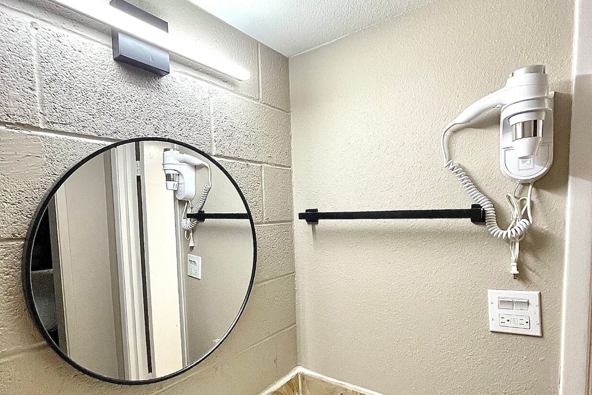 A bathroom with a round mirror, a sink, a towel rack, and a hairdryer mounted on the wall.