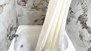 A bathroom with a white bathtub, a shower curtain, and a small window.