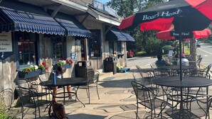 Une devanture de magasin avec des tables à l’extérieur, une enseigne indiquant « West Fallmouth Market » et un parapluie de la marque « Boar’s Head ».