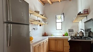 Cozinha compacta com geladeira de aço inoxidável, armários de madeira, piso ladrilhado e teto de madeira.