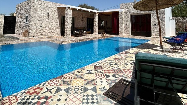 Uma área de piscina com paredes de pedra, um deck ladrilhado e móveis para exterior.