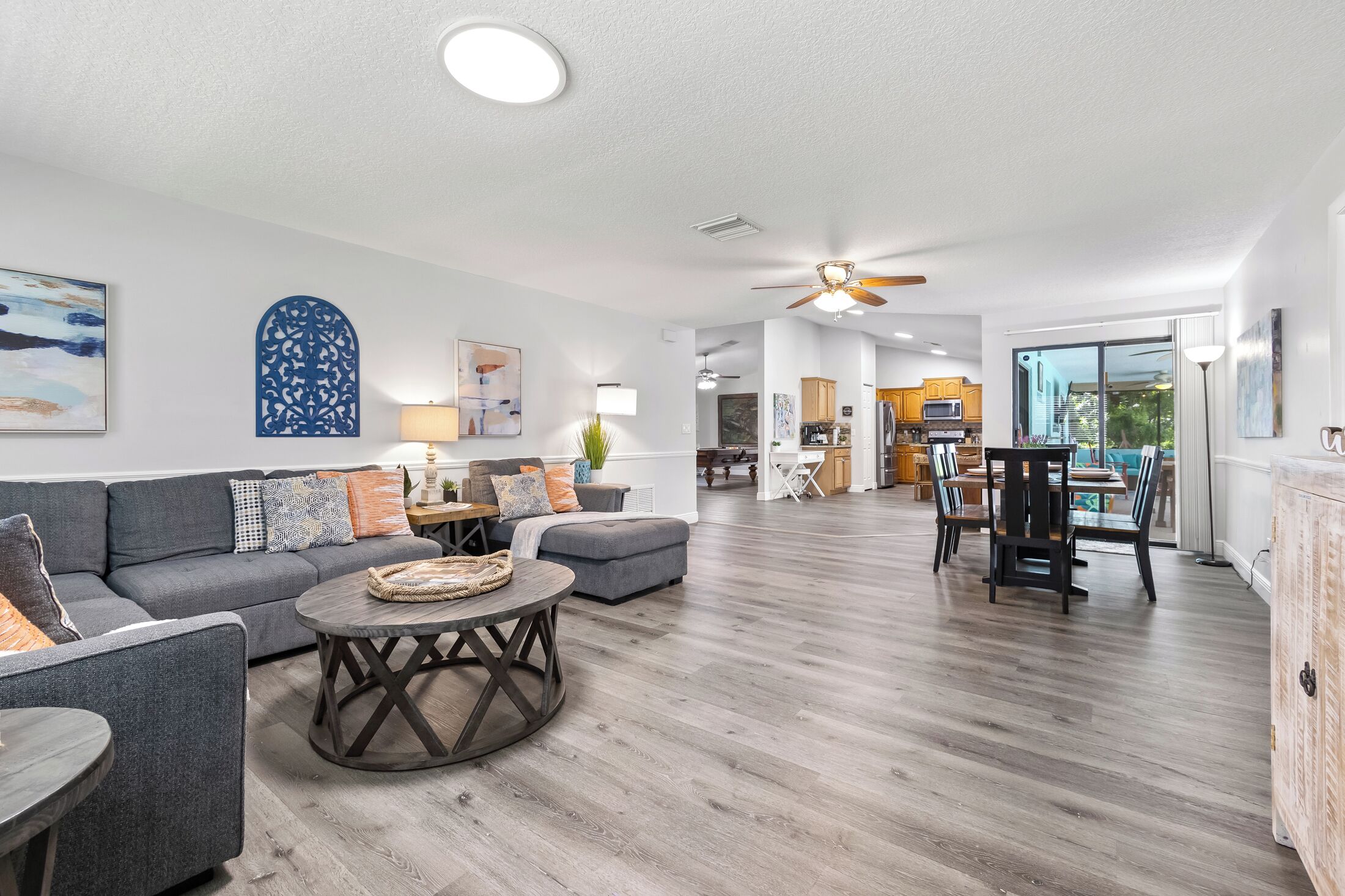 A spacious living room with a grey sofa, a round coffee table, and a dining area with a table and chairs.