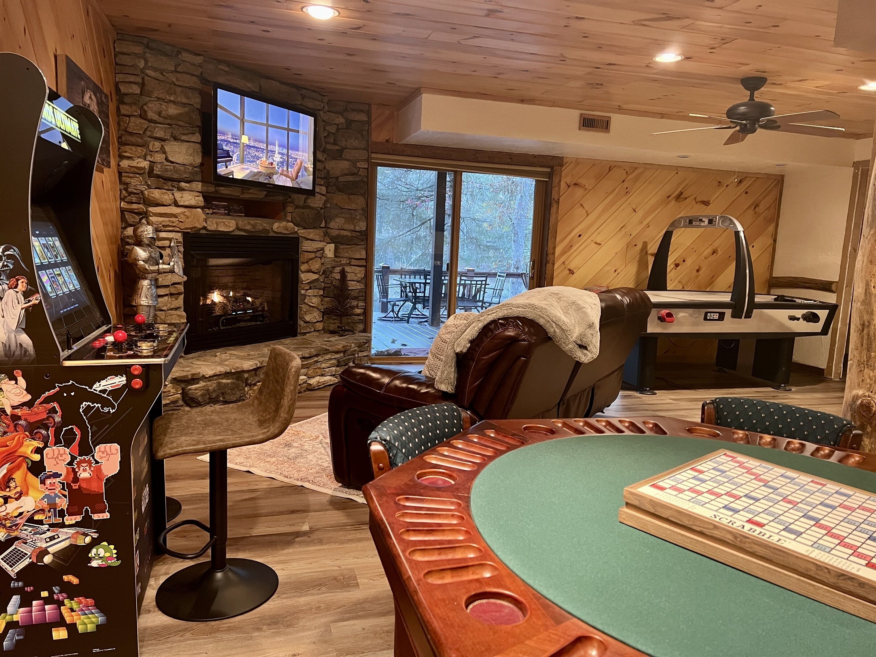 Un salon chaleureux avec une cheminée en pierre, une table de billard et une grande fenêtre donnant sur l’extérieur.