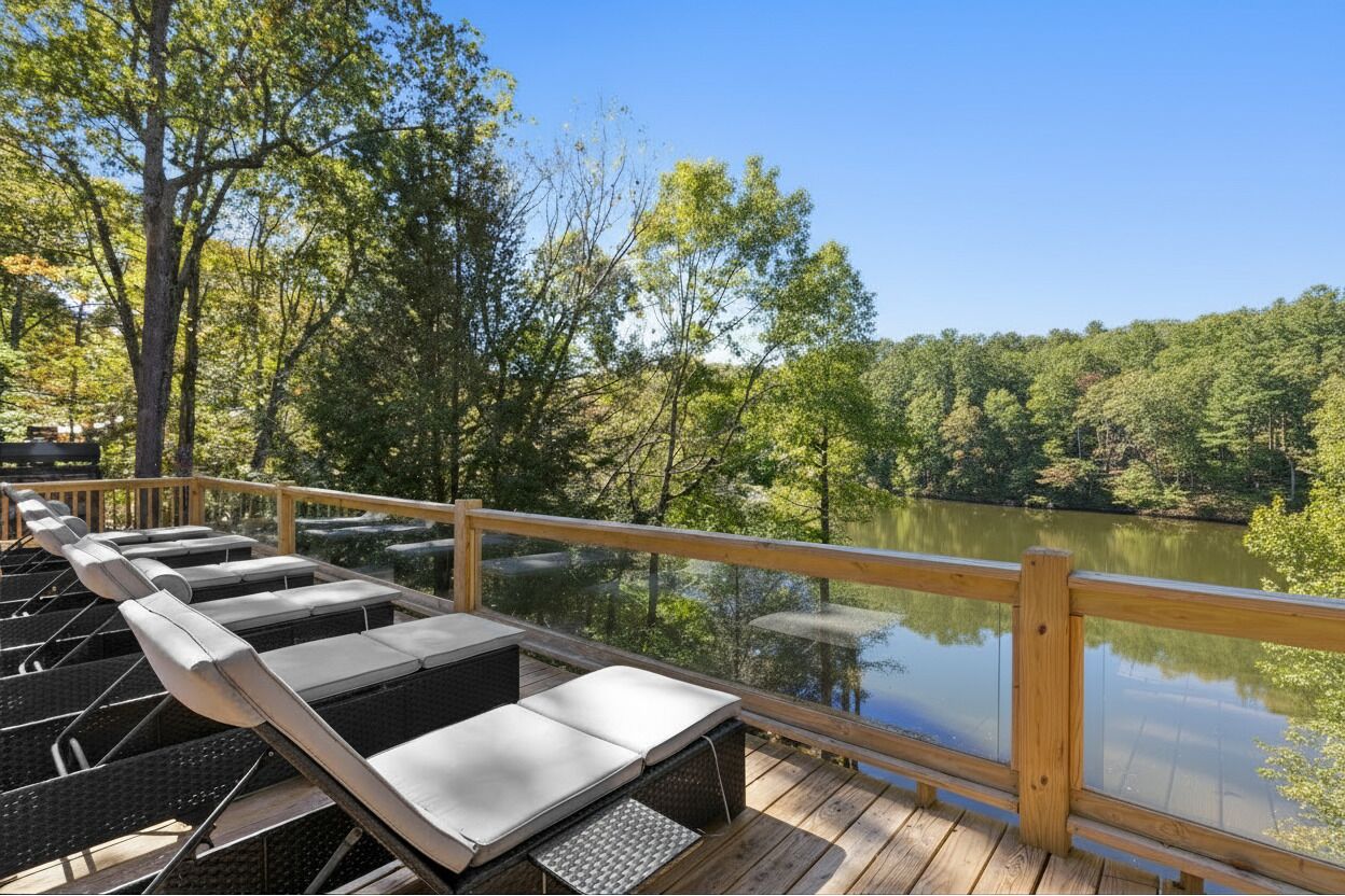 Una terraza de madera con sillones de descanso que da a un lago tranquilo, rodeada de árboles.