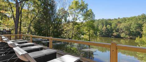 Una terraza de madera con sillones de descanso que da a un lago tranquilo, rodeada de árboles.