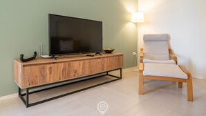 A modern living room with a flat-screen TV on a wooden TV stand, a light-colored armchair, and a floor lamp. - Sleek City Oasis - City Centre (Cagliari)