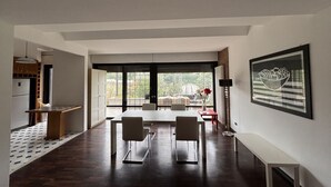 Un espace repas moderne avec une grande table et des chaises, un coin cuisine doté de placards et une vue dégagée grâce à de grandes fenêtres.