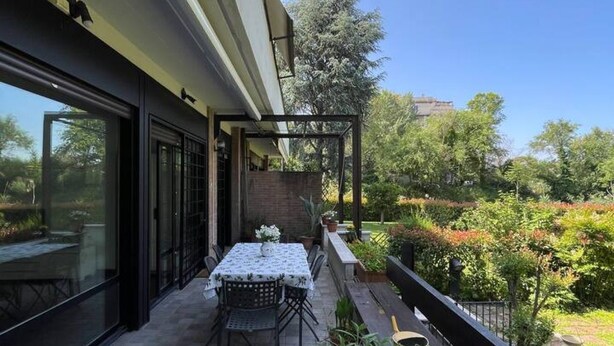 Une terrasse extérieure avec une table et des chaises, entourée d’une végétation luxuriante et sous un ciel dégagé.