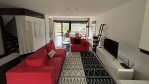 Un salon moderne avec un canapé rouge, un tapis à motifs noir et blanc, un téléviseur à écran plat et un escalier menant à un niveau supérieur.