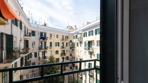 A view of a multi-story residential building with balconies, a clear sky, and a green railing in the foreground. - La Dolce Vita - IRIDE's Nest (Roma)