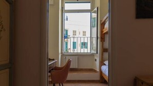 A narrow hallway with a window leading to a balcony. A chair is placed near the window, and a bed is visible in the background. - La Dolce Vita - IRIDE's Nest (Roma)